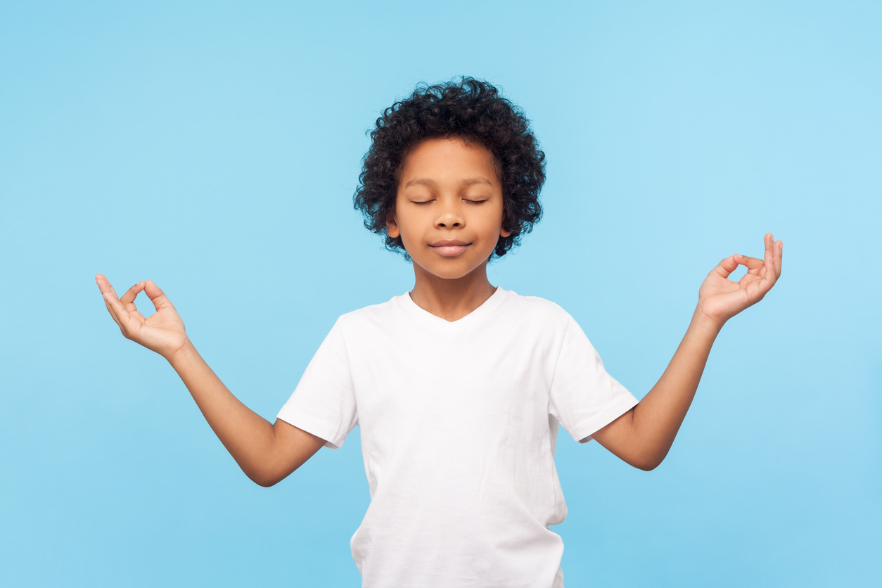 Portrait of peaceful cute little boy holding fingers in mudra gesture and meditating with closed eyes, feeling calm positive and relaxed, yoga practice. indoor studio shot isolated on blue background